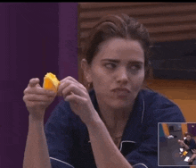 a woman in a blue shirt is holding a piece of food in her hand