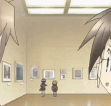 a couple of people are standing in a room with paintings on the wall .
