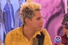 a man with blonde hair and a yellow shirt is sitting in front of a pink wall with a star on it .