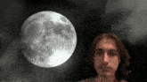 a young man stands in front of a full moon