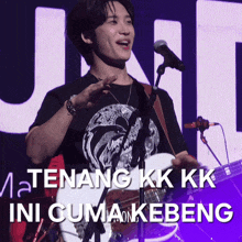 a man playing a guitar and singing into a microphone with the words " tenang kk kk ini cuma kebeng "
