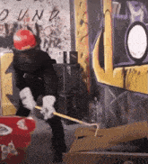 a man wearing a hard hat and gloves is holding a cane in front of a graffiti wall that says " own "