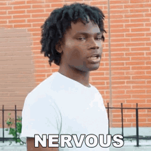 a man in a white shirt is standing in front of a brick wall with the word nervous written on his chest .