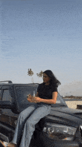 a woman is sitting on the hood of a car using her phone