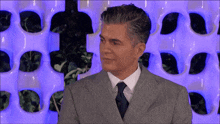 a man in a suit and tie is smiling in front of a purple wall