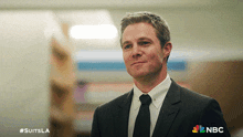 a man in a suit and tie is smiling with the nbc logo in the corner