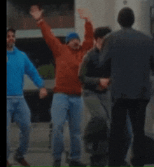 a man in a red jacket is standing in a crowd with his arms in the air