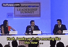 a group of people are sitting at a table with a sign that says leadership summit on it .