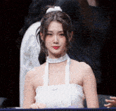 a woman wearing a white halter top with a clear strap around her neck looks at the camera
