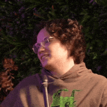 a woman wearing glasses and a brown hoodie with a green frog on it