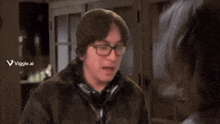 a man wearing glasses is making a funny face while sitting at a table in a dark room .
