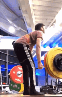a man lifts a barbell in a gym with a barbell that says ' oudu ' on the back