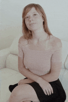 a woman sitting on a white couch wearing a pink off the shoulder top