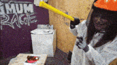 a woman wearing a hard hat is holding a yellow hammer in front of a wall that says mum rage