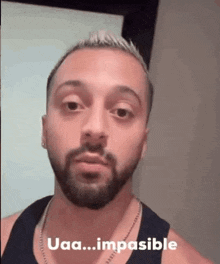 a man with a beard is wearing a black tank top and a necklace and is looking at the camera .