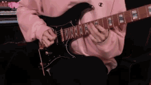 a person in a pink sweatshirt is playing a black electric guitar .