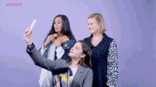 three women are taking a selfie together with a cell phone .