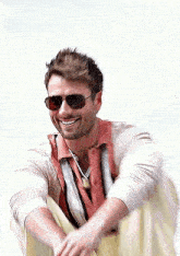 a man wearing sunglasses and a striped shirt is smiling while sitting down .