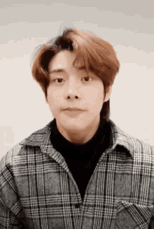 a close up of a young man wearing a plaid shirt and a black turtleneck .