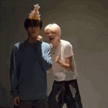 two men are standing next to each other and one of them is wearing a birthday hat .