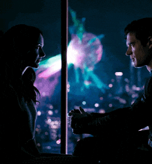 a man and woman looking at each other in front of a fireworks display