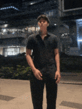 a young man in a black shirt is standing in front of a building at night .