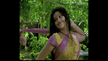 a woman in a pink and yellow top is smiling and holding her hair