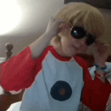 a person wearing sunglasses and a red and white shirt is sitting in a bed .