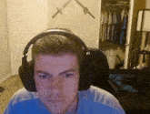 a man wearing headphones looks at the camera in a room with swords on the wall