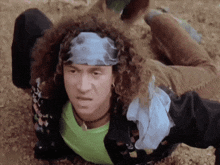 a man with curly hair wearing a bandana and earrings is laying on the ground