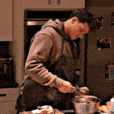 a man in an apron is cooking in a kitchen with a bowl .