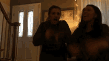 two women are standing in front of a door with a sign that says home