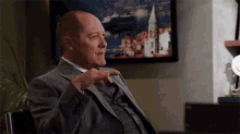 a man in a suit and tie is sitting in a chair in front of a painting .
