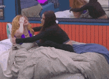 two women are sitting on a bed and one of them is covering her eyes