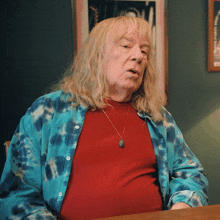 a man with long blonde hair is wearing a blue tie dye shirt