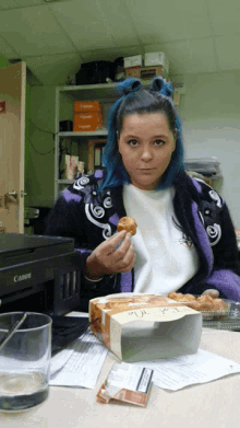 a woman sitting in front of a canon printer eating a pastry