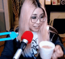 a woman with pink hair is holding a cup in front of a microphone .