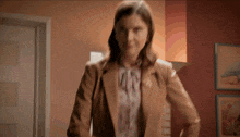a woman in a brown jacket is standing in front of a wall