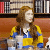 a woman with red hair is sitting at a table with a cup of coffee and a microphone .