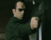a man in a suit and sunglasses is pointing a gun at something .