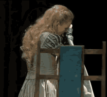 a woman in a blue dress sits in a chair with her hand on her face