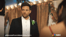 a man in a tuxedo with a flower in his lapel stands in front of a sign that says nbc