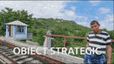 a man in a striped shirt stands on a bridge over train tracks with the words object strategic written below him