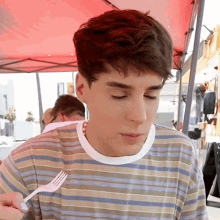 a young man in a striped shirt is eating with a fork
