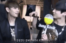 two young men are standing next to each other and one of them is holding a yellow lollipop that says jung kook .