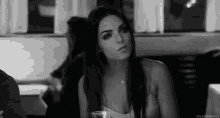 a black and white photo of a woman sitting at a table in a restaurant with a glass of wine .