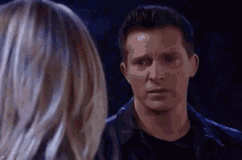 a man and a woman are looking at each other in a dark room . the man is wearing a leather jacket .