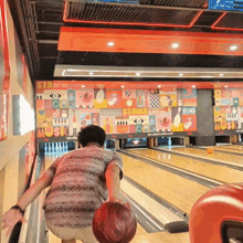a man throws a bowling ball at a bowling alley with a strike sign on the wall behind him