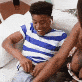a man in a blue and white striped shirt is sitting on a couch while a woman holds his pants down .