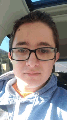 a man wearing glasses and a blue sweatshirt looks down at the camera
